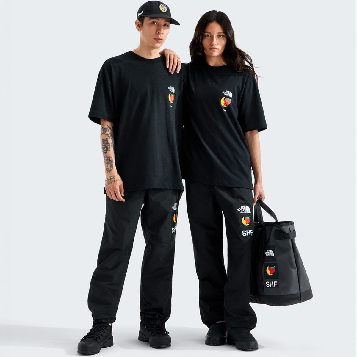 Two people wearing matching black outfits with logos, standing against a white background.
